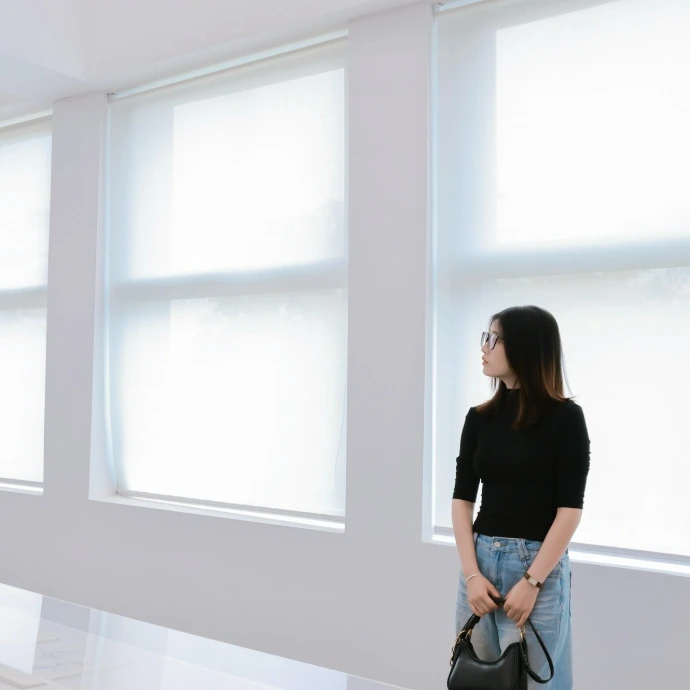 A woman stands by large windows in a bright room
